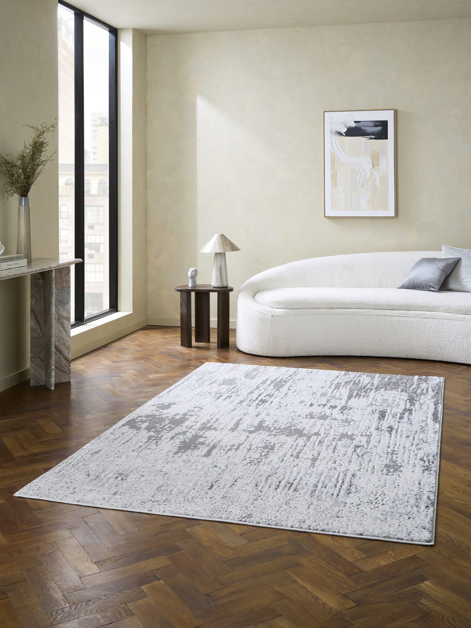 Apollo rectangular rug in grey and silver, in front of a pale curved sofa.