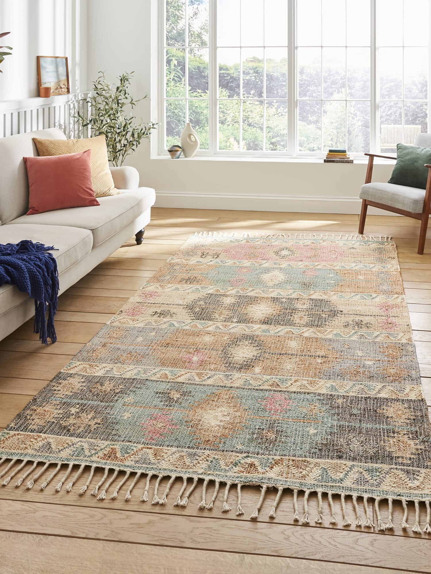 Bazaar Diamond Bands Multi Hand-Woven Rug. Bazaar Diamond Bands rectangular rug in mixed colours, between a pale sofa and a window.