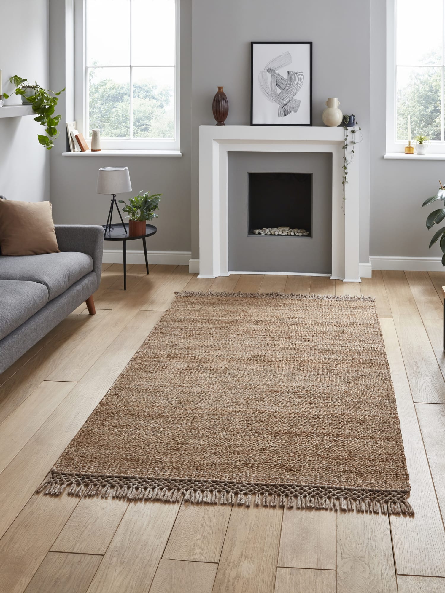 Bazaar Tonal Stripe rectangular rug in natural, in front of a fireplace beside a grey sofa.