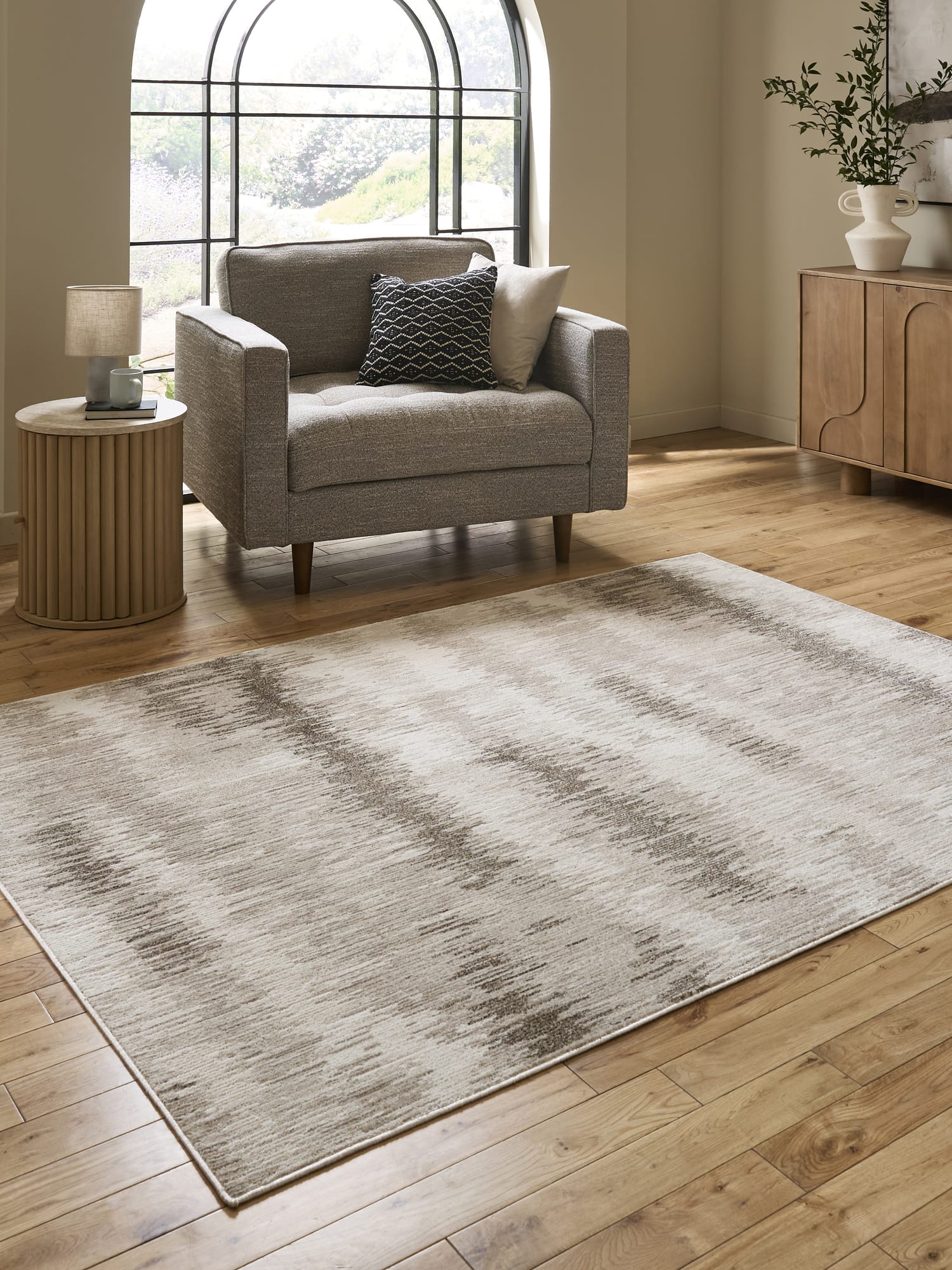 Drift rectangular rug in cream and beige, beside an armchair and an arched window.