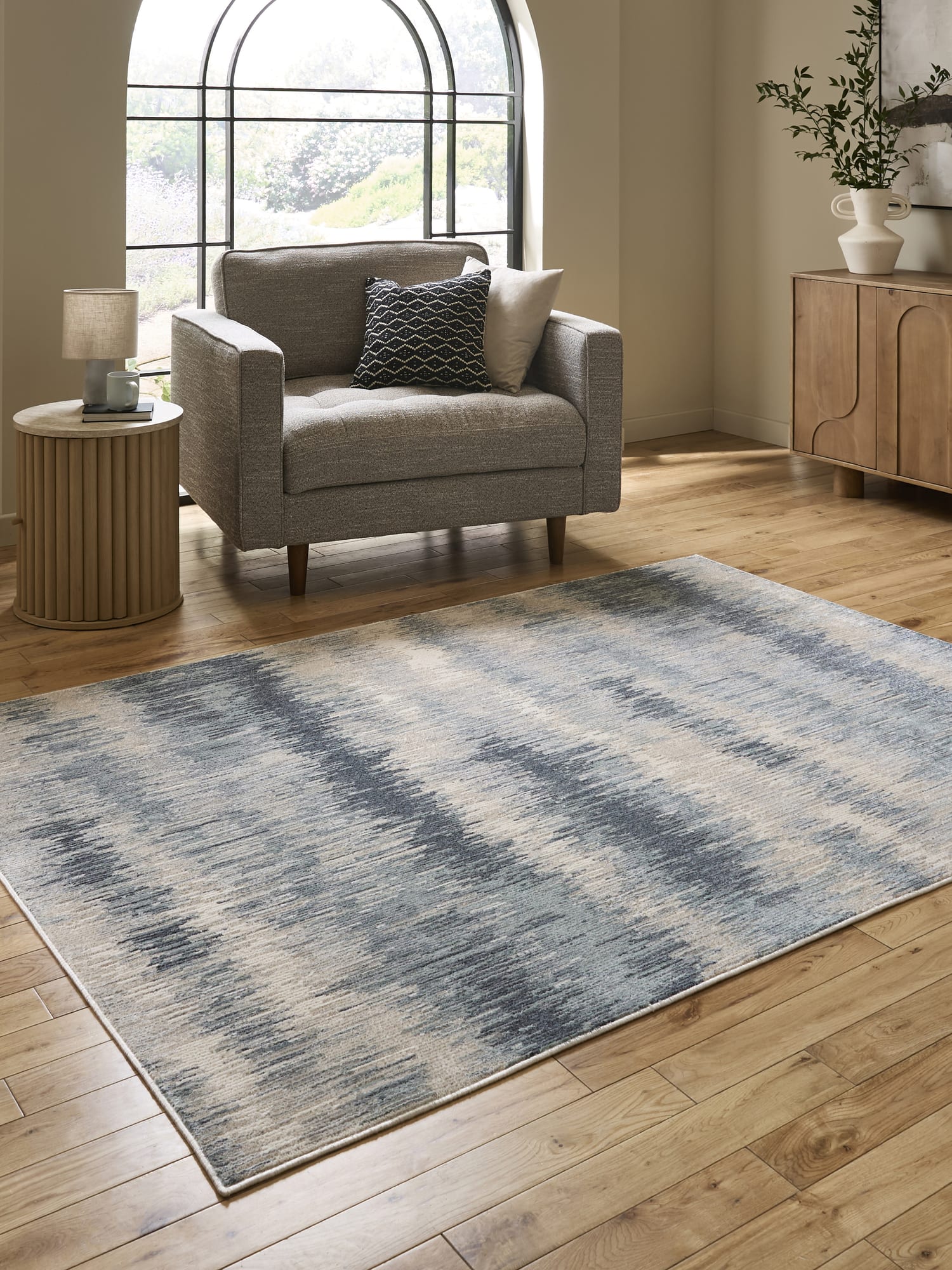 Drift rectangular rug in cream and blue, beside an armchair and an arched window.