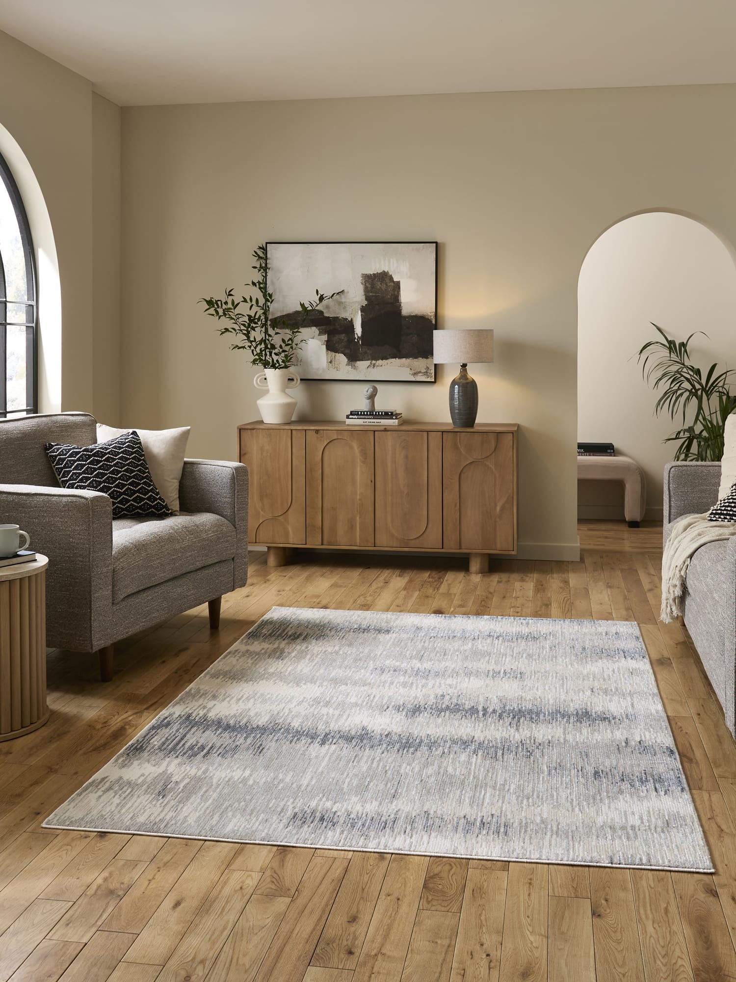 Drift rectangular rug in cream and grey, in a room with a wooden sideboard and pale walls.