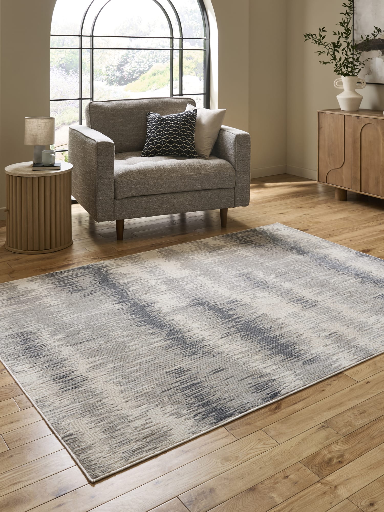 Drift rectangular rug in cream and grey, beside an armchair and an arched window.