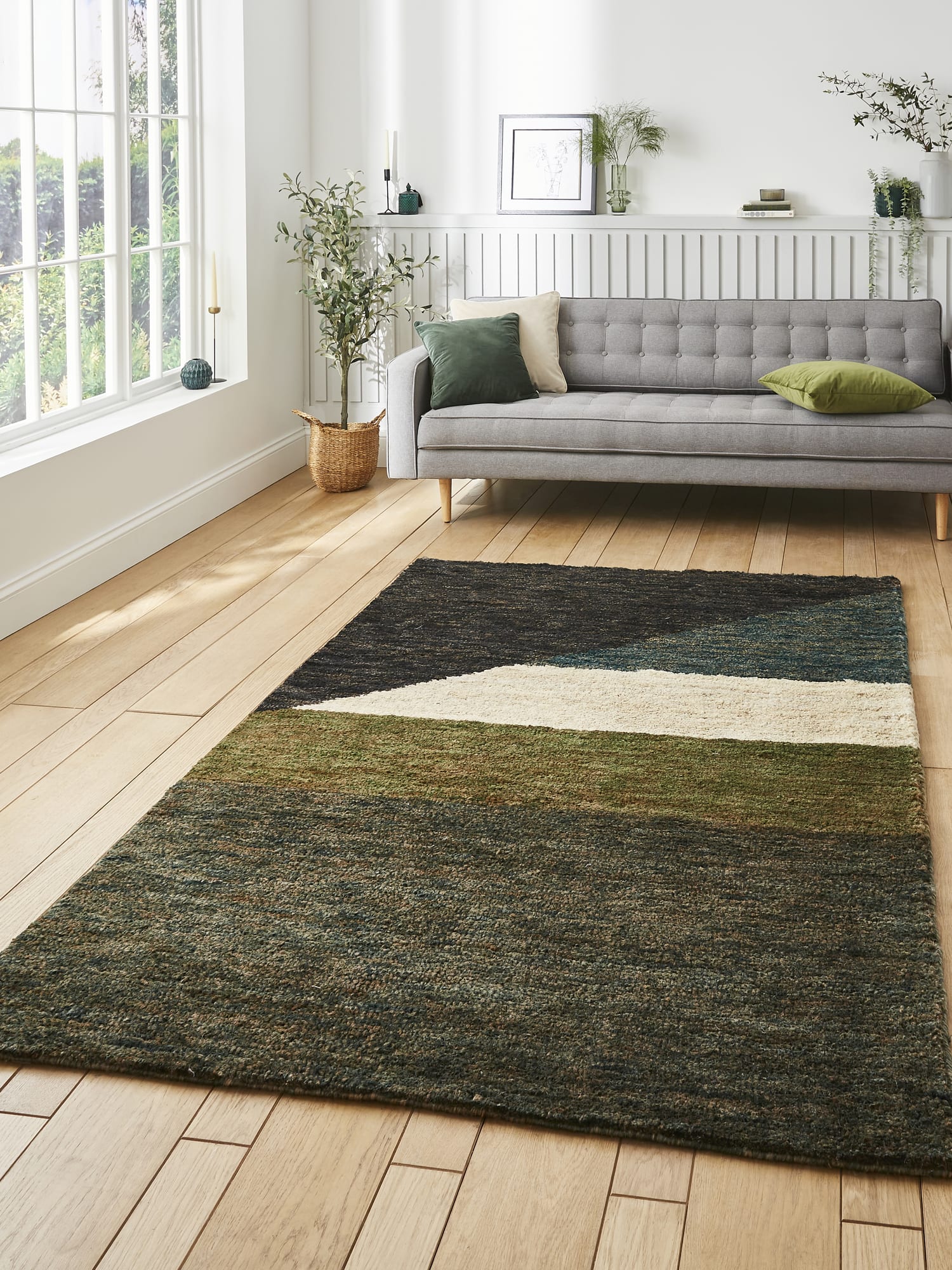 Hemp Multi Hand-Knotted Rug. Hemp rectangular rug in charcoal, teal, olive and cream, beside a grey sofa and large windows.