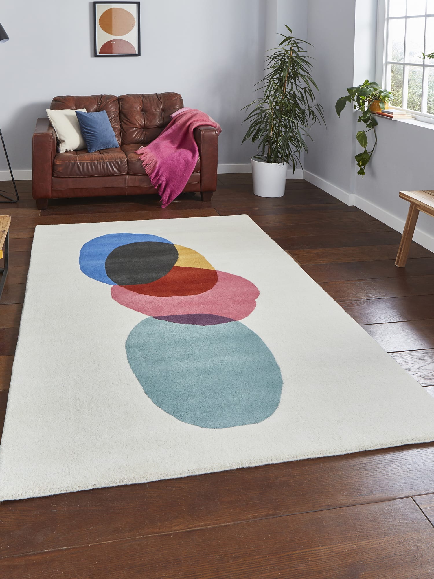 Inaluxe Transmission rectangular rug in cream with blue, pink, yellow, red, teal and dark shapes, in front of a brown sofa.