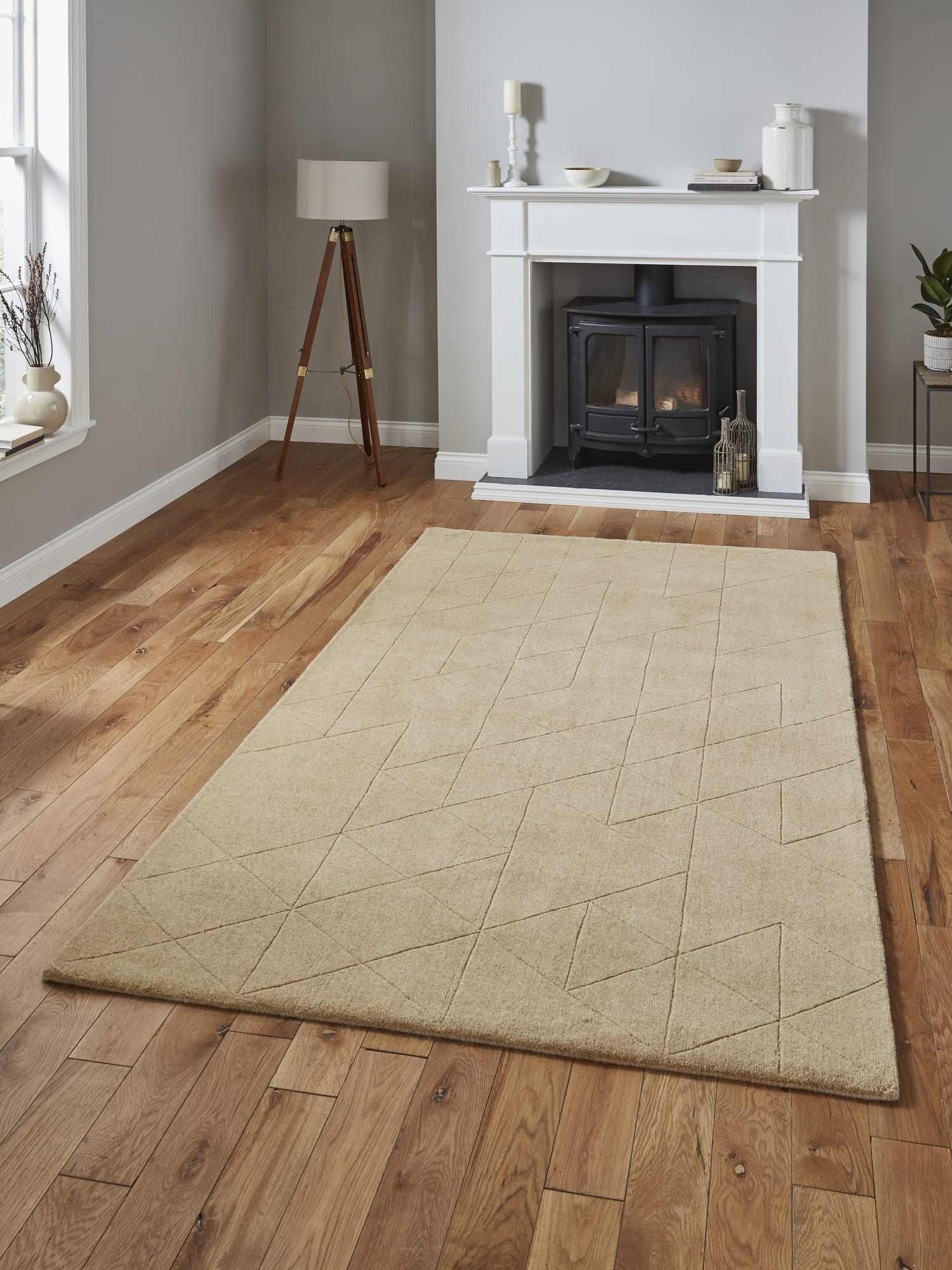 Kasbah rectangular rug in beige, on a wooden floor in front of a fireplace.
