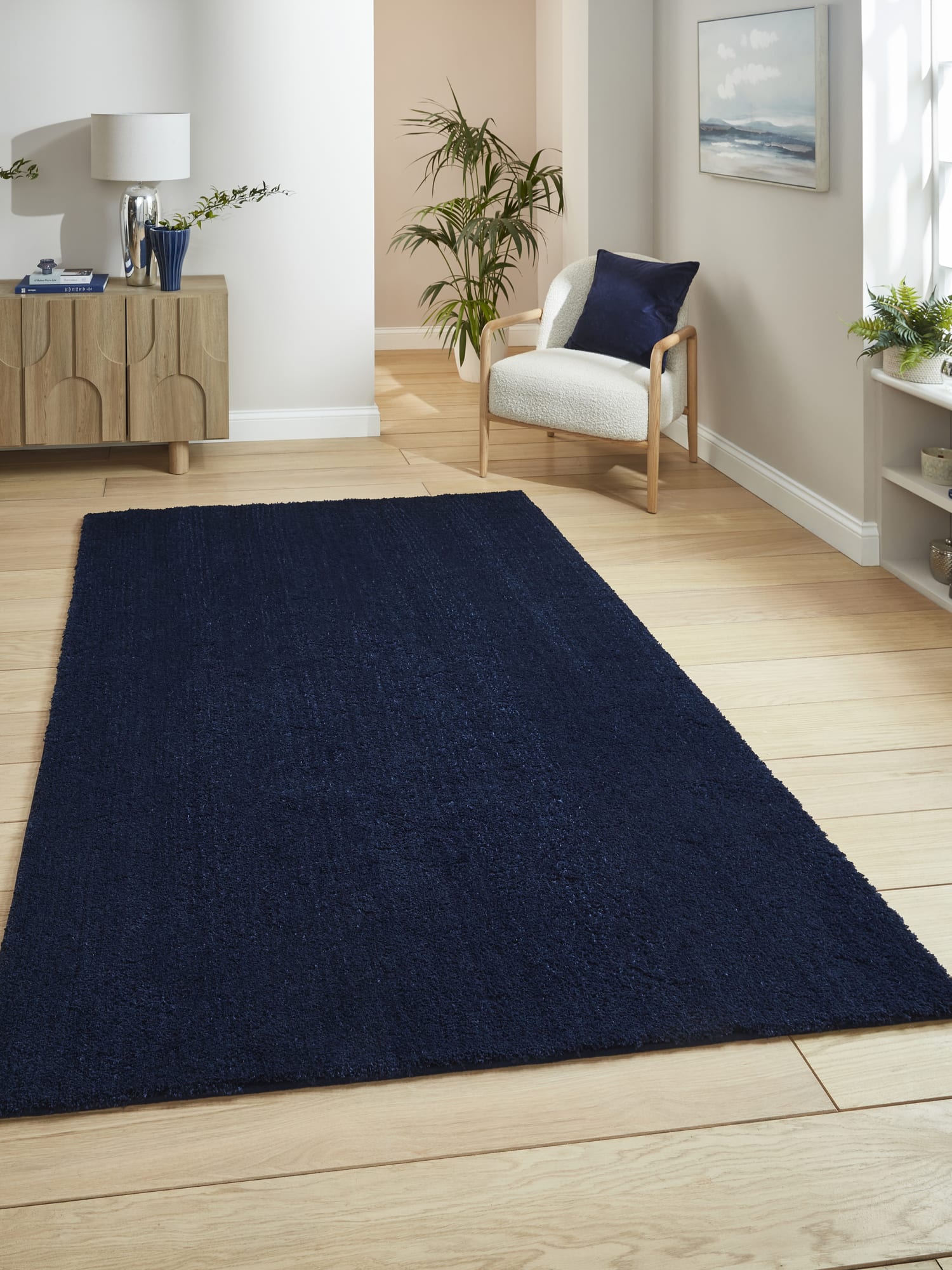 Riviera rectangular rug in navy, beside an armchair and a wooden cabinet.