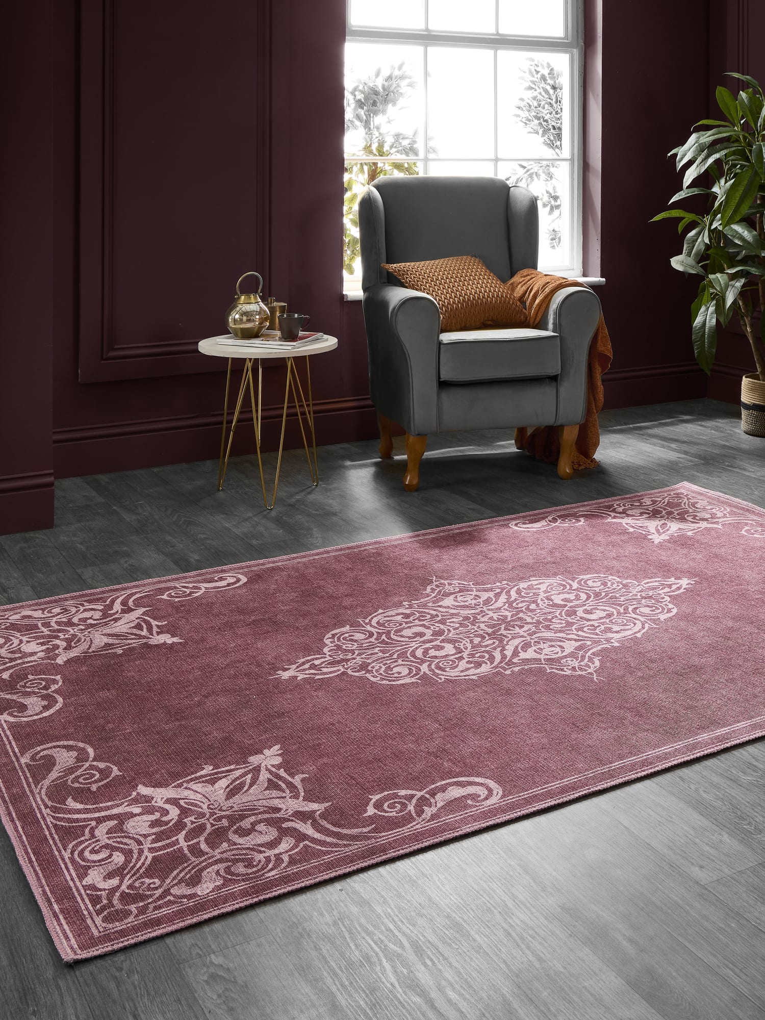 Sarabande rectangular rug in red, at an angle beside an armchair in a dark-walled room.