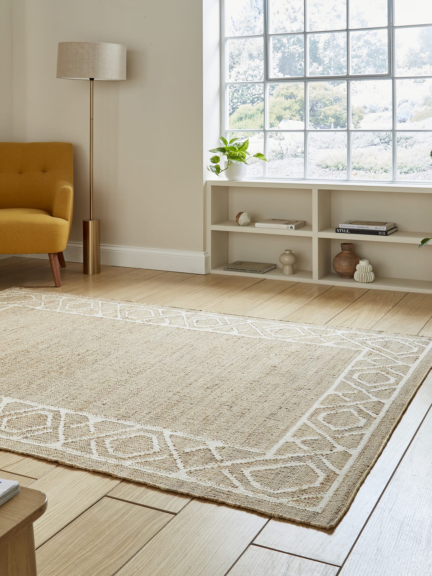 Spartan Diamond Border rectangular rug in natural and ivory, at an angle beside a large window.