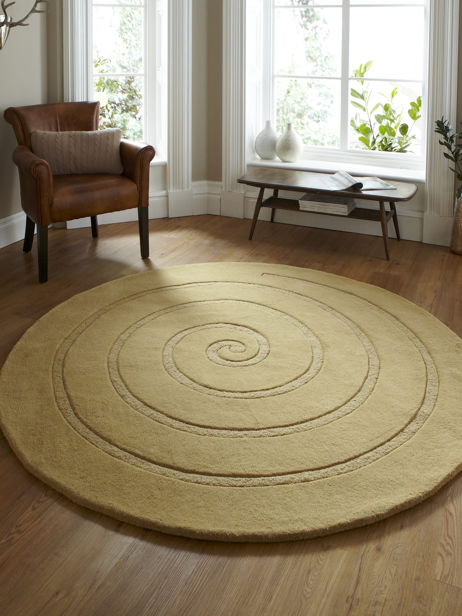 Spiral round rug in gold, beside a brown armchair and a window.