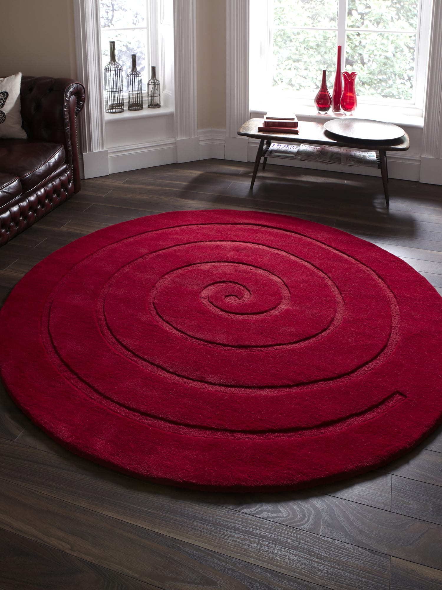 Spiral round rug in red, beside a dark sofa and a window.