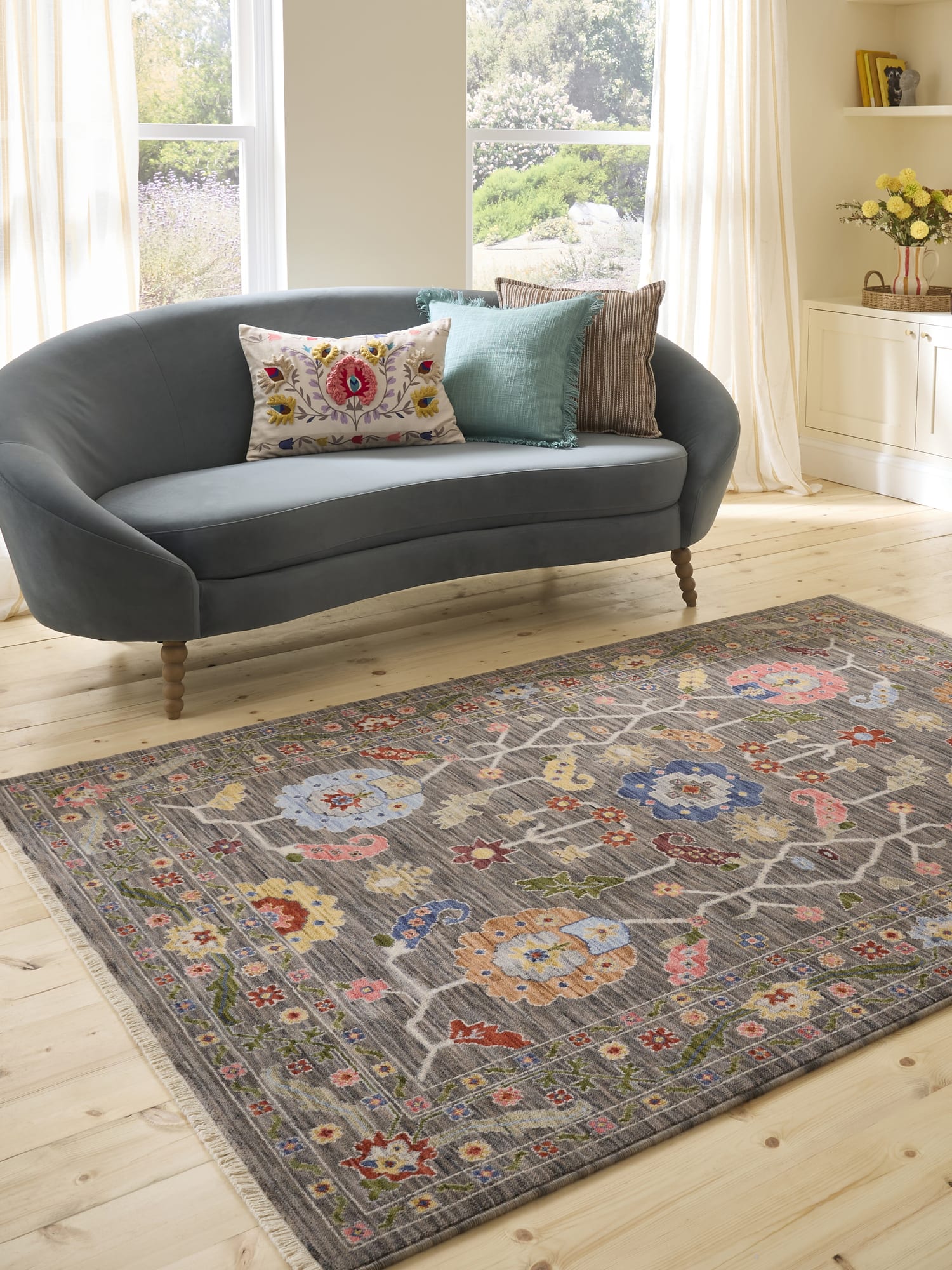 Suzani Branching Floral Black/Multi Wool-Blend Rug. Suzani Branching Floral rectangular rug in black and mixed colours, beside a dark curved sofa.