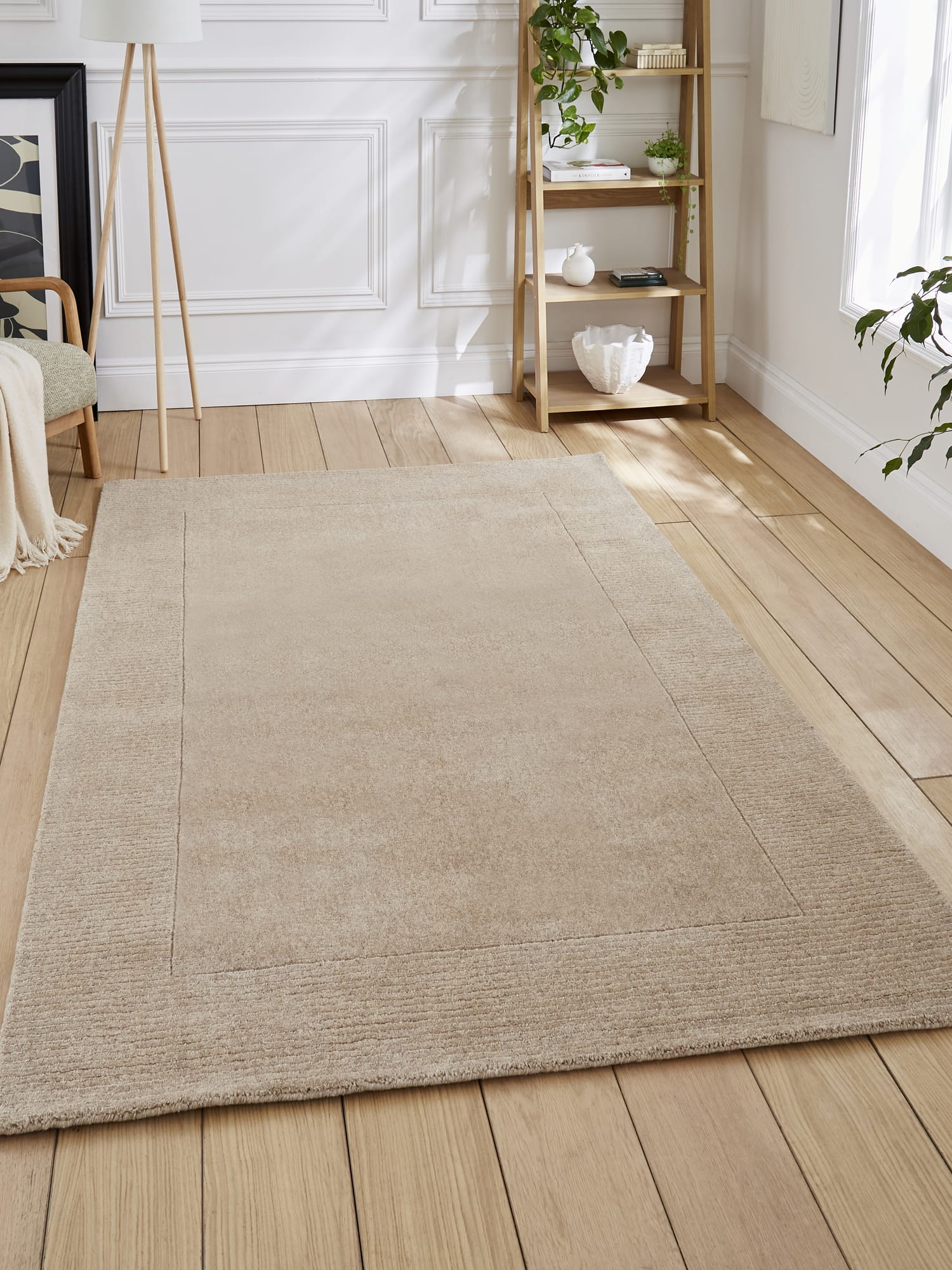 Windsor Border rectangular rug in natural, on a wooden floor beside open shelving.