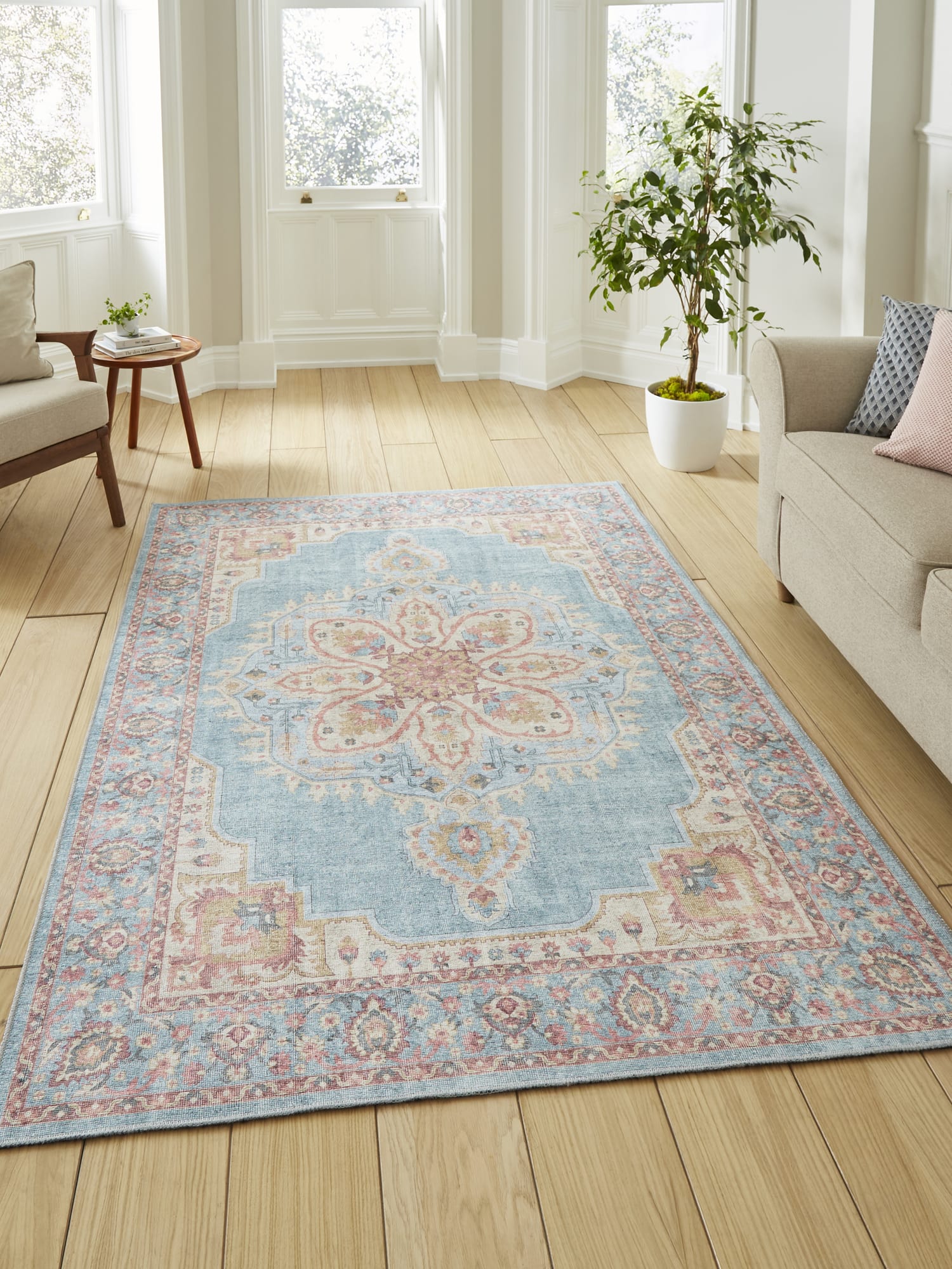 Zahra Washable rectangular rug in blue and beige, beside a pale sofa and tall windows.