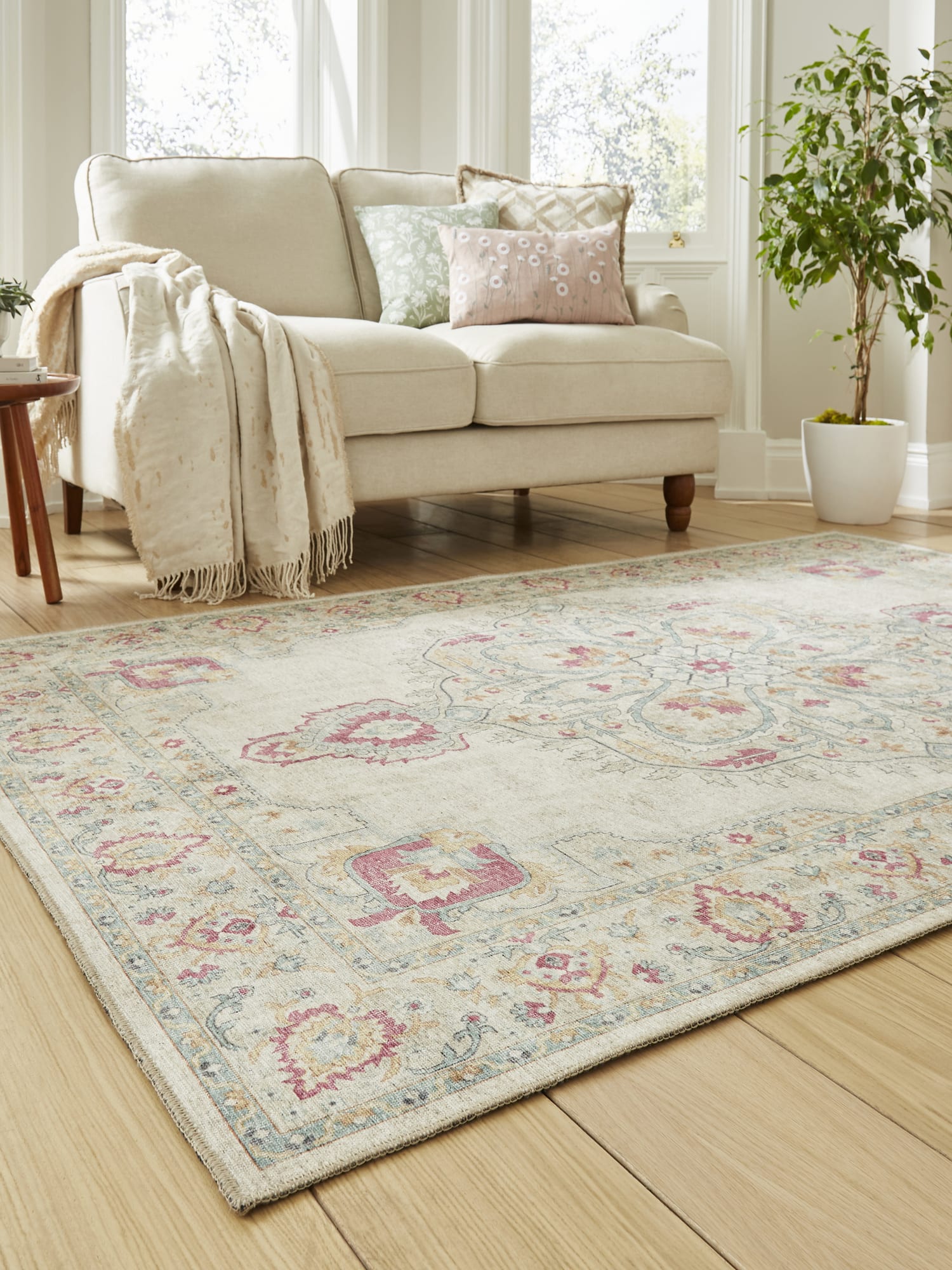 Zahra Washable rectangular rug in cream, at an angle beside a pale sofa.