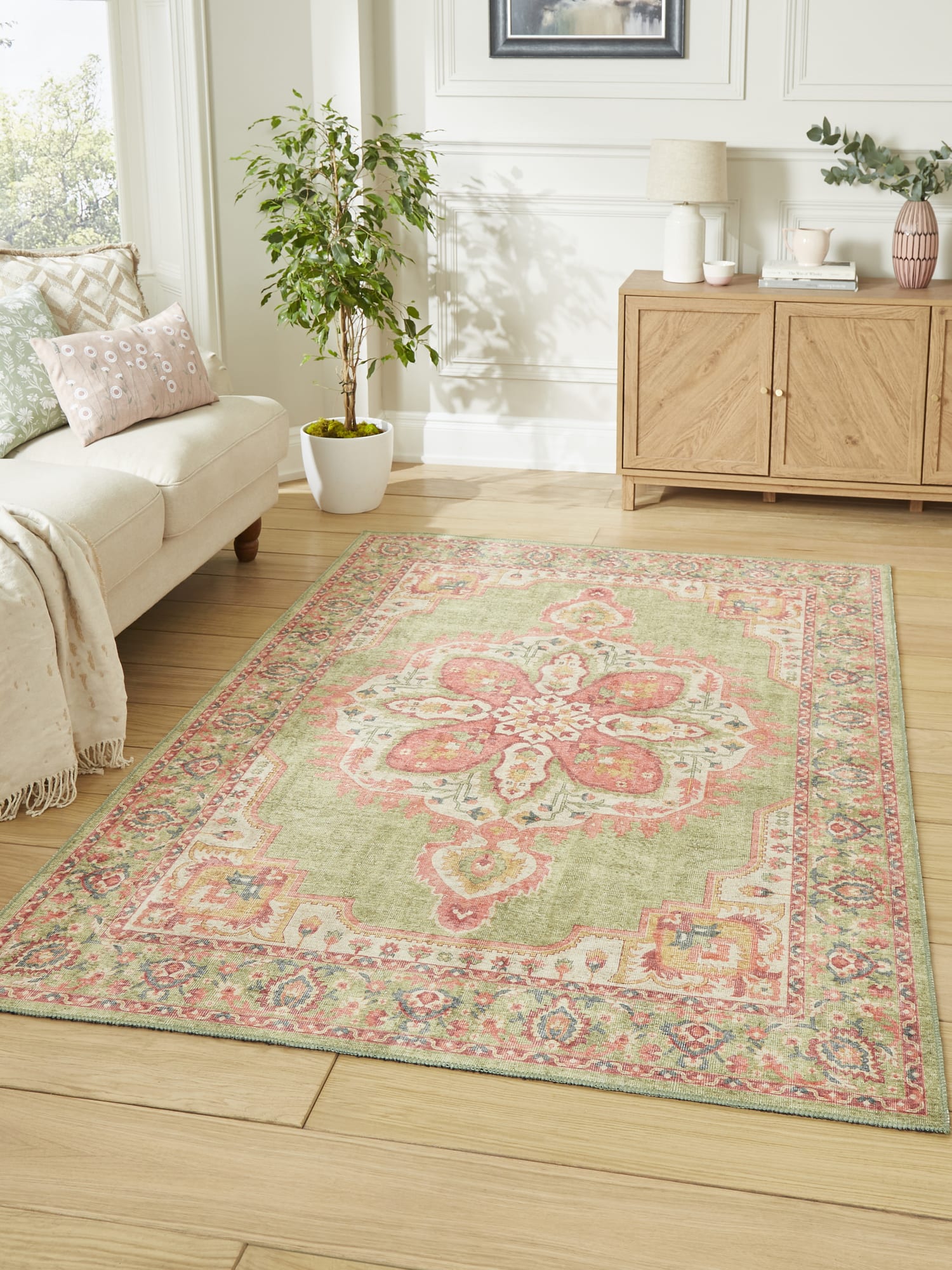 Zahra Washable rectangular rug in green and pink, beside a pale sofa and a wooden cabinet.