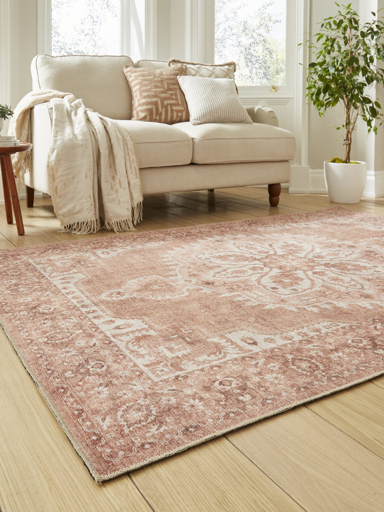 Zahra Washable rectangular rug in terracotta, at an angle beside a pale sofa.