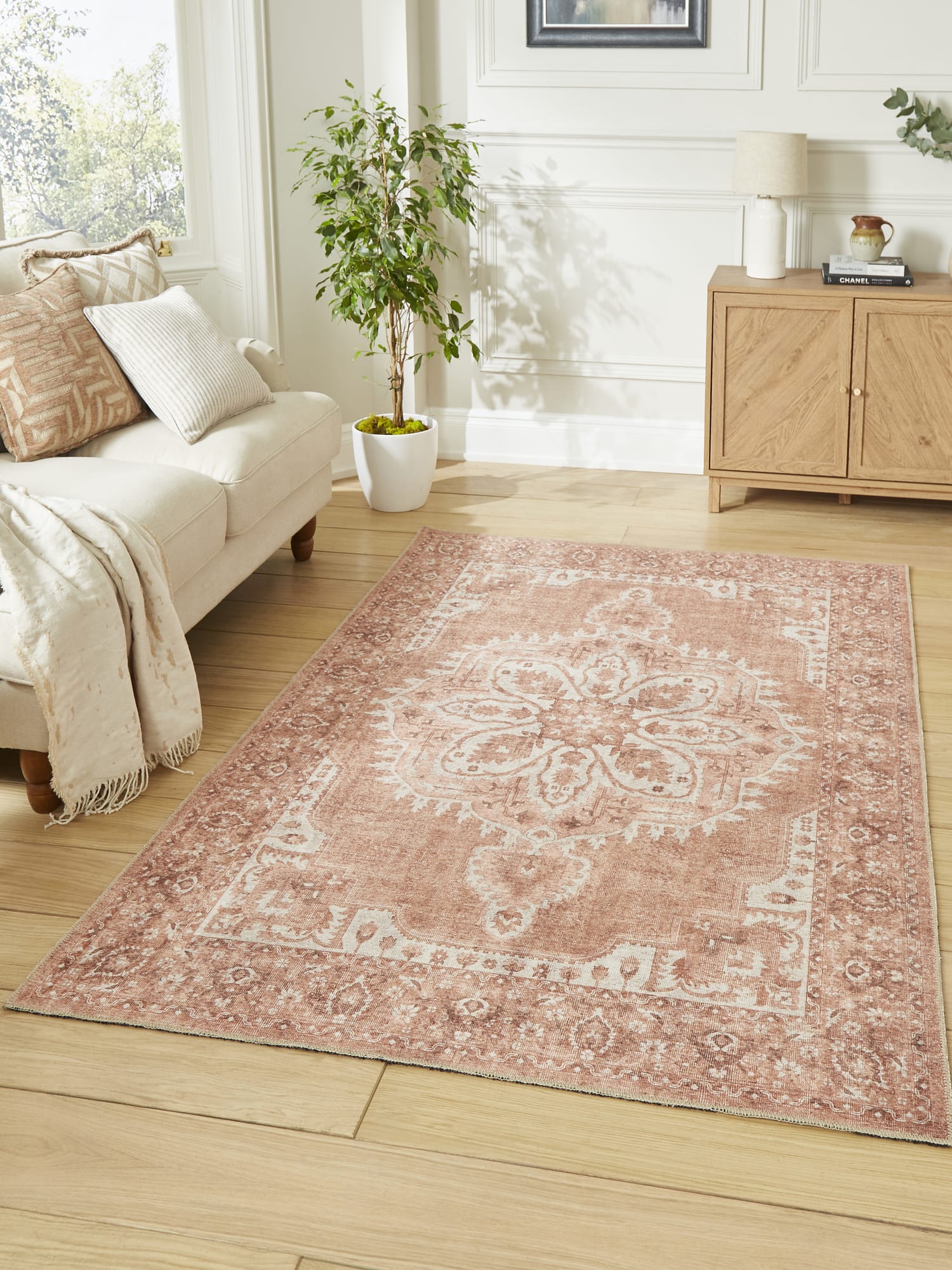 Zahra Washable rectangular rug in terracotta, beside a pale sofa and a wooden cabinet.